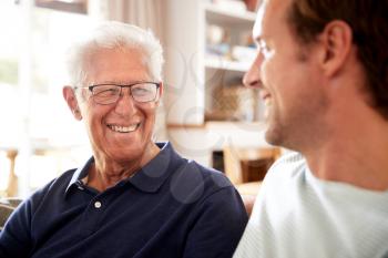 Smiling Father With Adult Son Relaxing On Sofa At Home