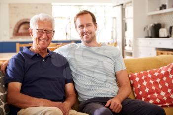 Portrait Of Smiling Father With Adult Son Relaxing On Sofa At Home