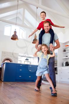 Daughter Playing Game Walking On Fathers Feet With Son On Shoulders At Home