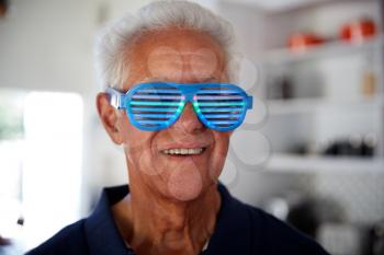 Senior Man At Home Wearing Novelty Party Glasses