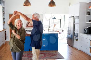 Senior Couple At Home Dancing In Kitchen Together