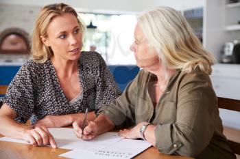 Female Friend Helping Senior Woman To Complete Last Will And Testament At Home