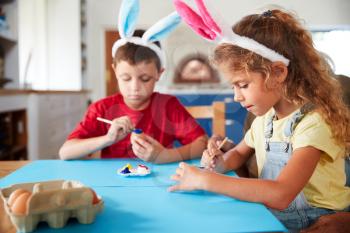 Children Wearing Rabbit Ears Decorating Easter Eggs At Home Together