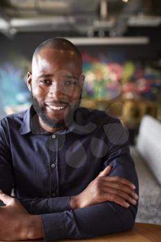 Mid adult black male creative sitting at a table in an office cafe smiling to camera, close up, crop