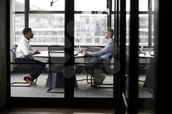 A black and a white businessman meeting for a job interview, full length, seen through glass wall