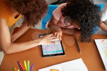 Elementary School Teacher And Female Pupil Drawing Using Digital Tablet In Classroom