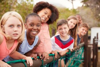 Portrait Of Children Standing On Rope Bridge With Friends In Park