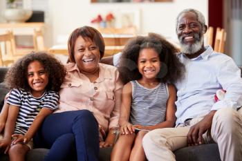 Portrait Of Smiling Grandparents With Grandchildren Sitting On Sofa At Home Relaxing Together