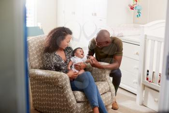 Loving Parents Sitting In Chair Cuddling Baby Son In Nursery At Home