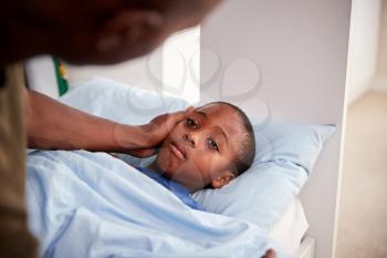 Father Caring For Sick Son Lying  Ill In Bed At Home
