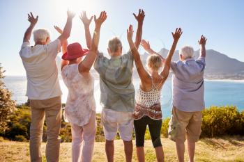 Rear View Of Senior Friends Visiting Tourist Landmark On Group Vacation With Arms Raised