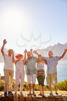 Portrait Of Senior Friends Visiting Tourist Landmark On Group Vacation With Arms Raised