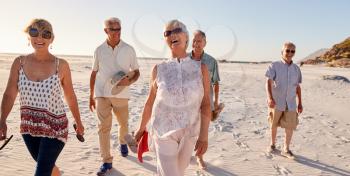 Group Of Senior Friends Walking Along Sandy Beach On Summer Group Vacation