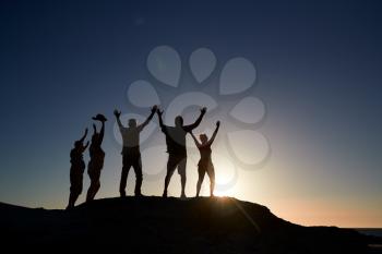 Silhouette Of Senior Friends Standing On Rocks By Sea On Vacation At Sunset With Arms Outstretched