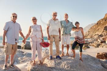 Portrait Of Senior Friends Standing On Rocks By Sea On Summer Group Vacation