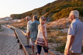 Group Of Senior Friends Walking Along Boardwalk At Beach On Summer Group Vacation