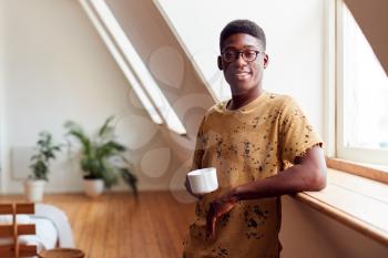 Portrait Of Young Man Relaxing In Loft Apartment With Hot Drink