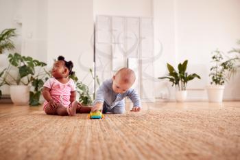 Baby Boy And Girl Playing With Toys On Rug At Home Together