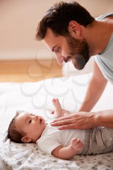 Loving Father Lying With Newborn Baby On Bed At Home In Loft Apartment