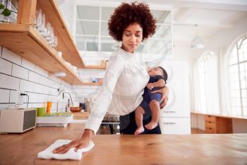 Multi-Tasking Mother Holds Sleeping Baby Son And Cleans In Kitchen