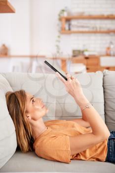 Woman Relaxing Lying On Sofa At Home Looking At Digital Tablet