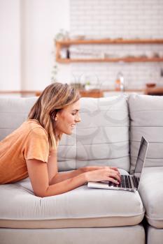 Woman Relaxing Lying On Sofa At Home Using Laptop Computer