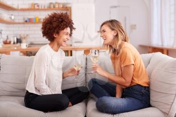 Two Female Friends Relaxing On Sofa At Home With Glass Of Wine Talking Together