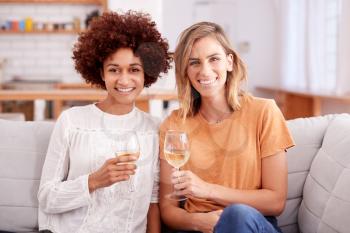 Portrait Of Two Female Friends Relaxing On Sofa At Home With Glass Of Wine Talking Together