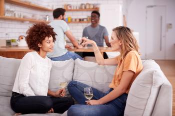 Two Couples Relaxing On Sofa At Home With Glass Of Wine Talking Together