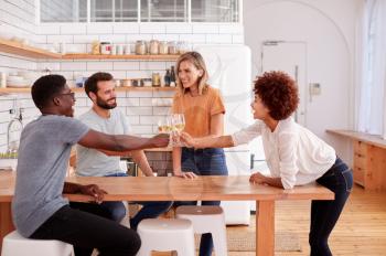 Two Couples Relaxing In Kitchen At Home Making A Toast With Glass Of Wine Together