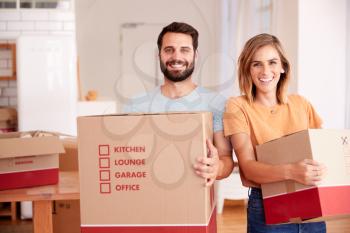 Portrait Of Smiling Couple Carrying Boxes Into New Home On Moving Day