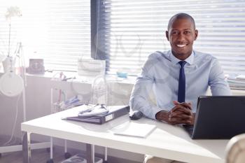 Portrait Of Smiling Male Doctor Sitting Behind Desk In Office