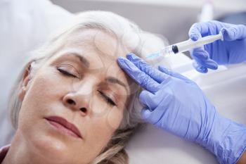Beautician Giving Mature Female Patient Botox Injection In Forehead