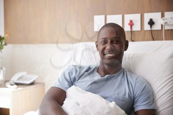 Portrait Of Male Patient Lying In Hospital Bed Smiling At Camera