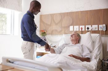 Doctor Shaking Hands With Senior Male Patient In Hospital Bed In Geriatric Unit