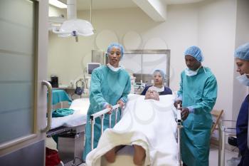 Surgical Team Wheeling Senior Male Patient Out Of Hospital Operating Theatre