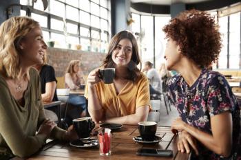 Three Young Female Friends Meeting Sit At Table In Coffee Shop And Talk