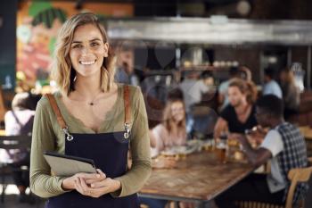 Portrait Of Waitress Holding Menus Serving In Busy Bar Restaurant