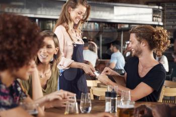 Waitress Holds Credit Card Machine As Customer Pays Bill In Bar Restaurant