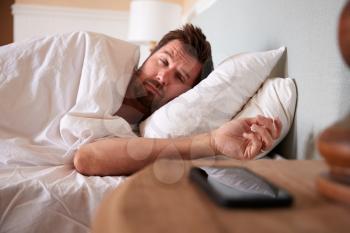 Mid adult man asleep in bed, looking at the smartphone on the bedside table in the foreground