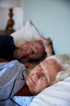 Senior white couple asleep in their bed, waist up, close up, vertical