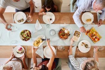 Three generation white family sitting at a dinner table together serving a meal, overhead view