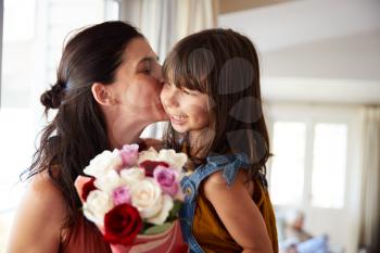Mid adult woman kissing her daughter, who’s given her a bunch of flowers on her birthday, close up
