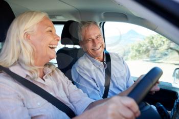 Senior white woman and her husband driving in their car laughing together, close up, side view