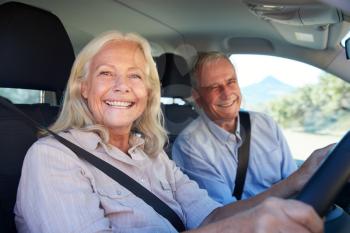 Senior white woman and her husband driving in their car smiling to camera, close up, side view