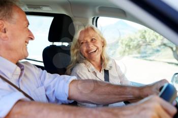 Senior white couple driving in their car, looking at each other, side view, close up