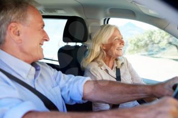Happy senior white couple driving in their car, smiling, side view, close up