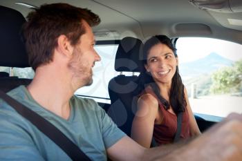 Happy mid adult white couple driving in their car, smiling at each other, close up, side view