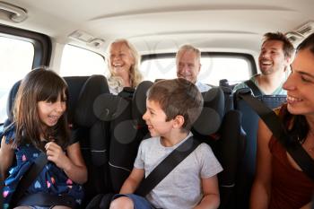 Three generation white family sitting in two rows of passenger seats in a car, looking at each other