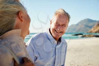 Senior white couple walking on a beach, looking at each other and smiling, waist up, close up
